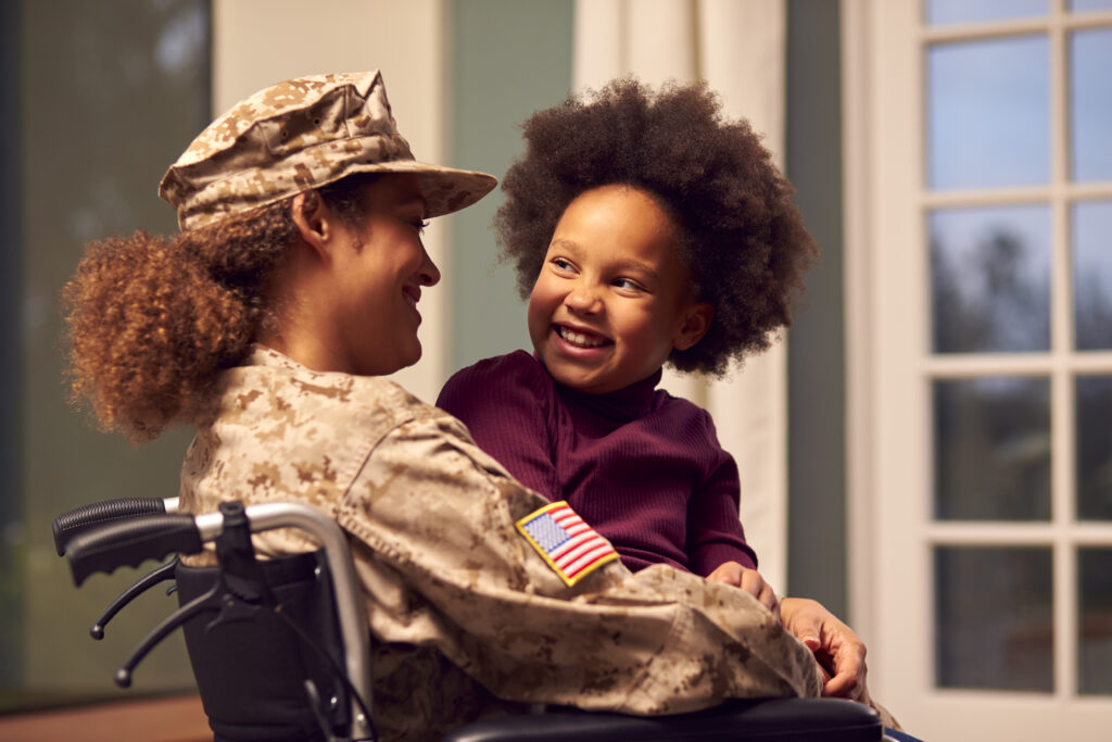 Injured Woman Soldier Sitting In Wheelchair Hugging Daughter